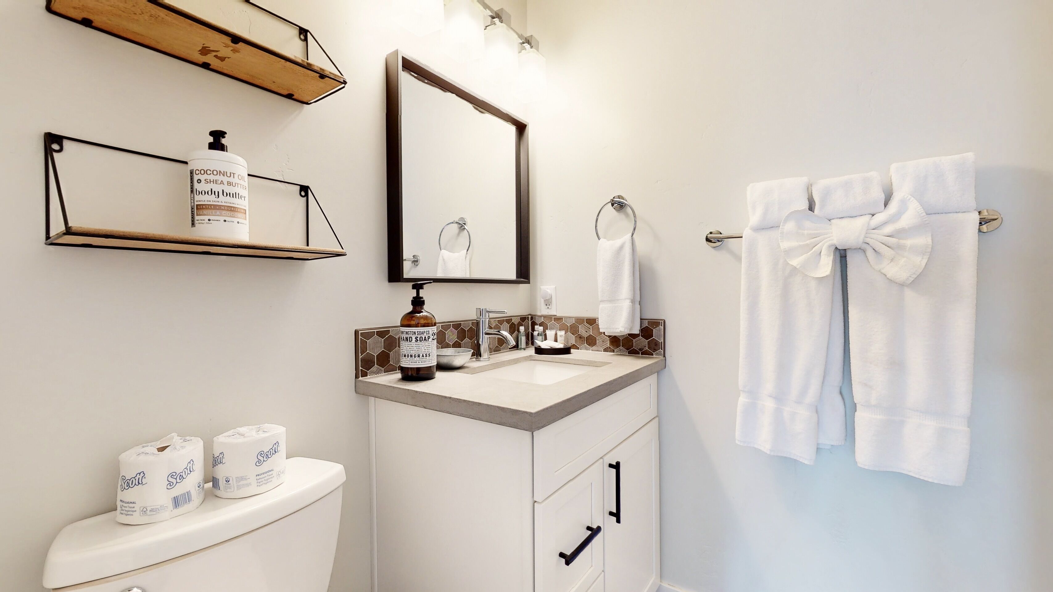 A bathroom with a toilet, sink, and mirror. There are towels and toiletries on the counter.