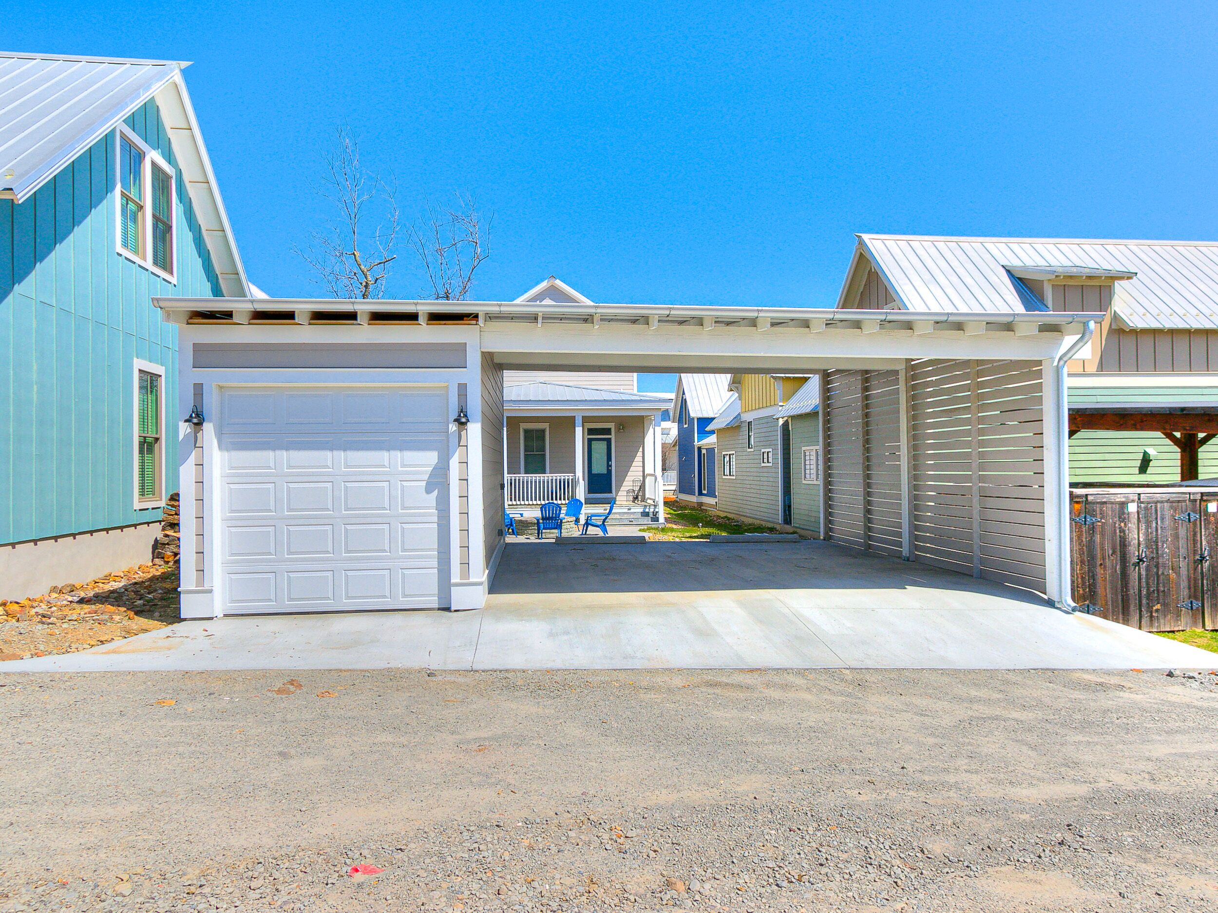 A residential driveway with a garage, a covered porch, and a small front yard with a chair.