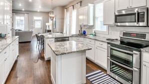 A modern kitchen with white cabinetry, granite countertops, stainless steel appliances, and a central island. - Carlton Landing! Charming Cottage on boardwalk! (Carlton Landing)