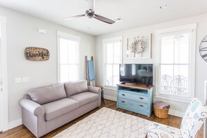 A living room with a grey sofa, a TV on a wooden stand, a blue dresser, and a patterned rug.