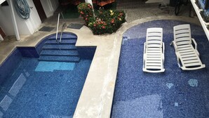 Una piscina con escalones de acceso, un área de descanso con tumbonas y un pequeño jardín con flores.