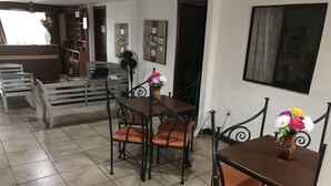 Un comedor con una mesa marrón y cuatro sillas, un florero blanco con flores y un abanico.