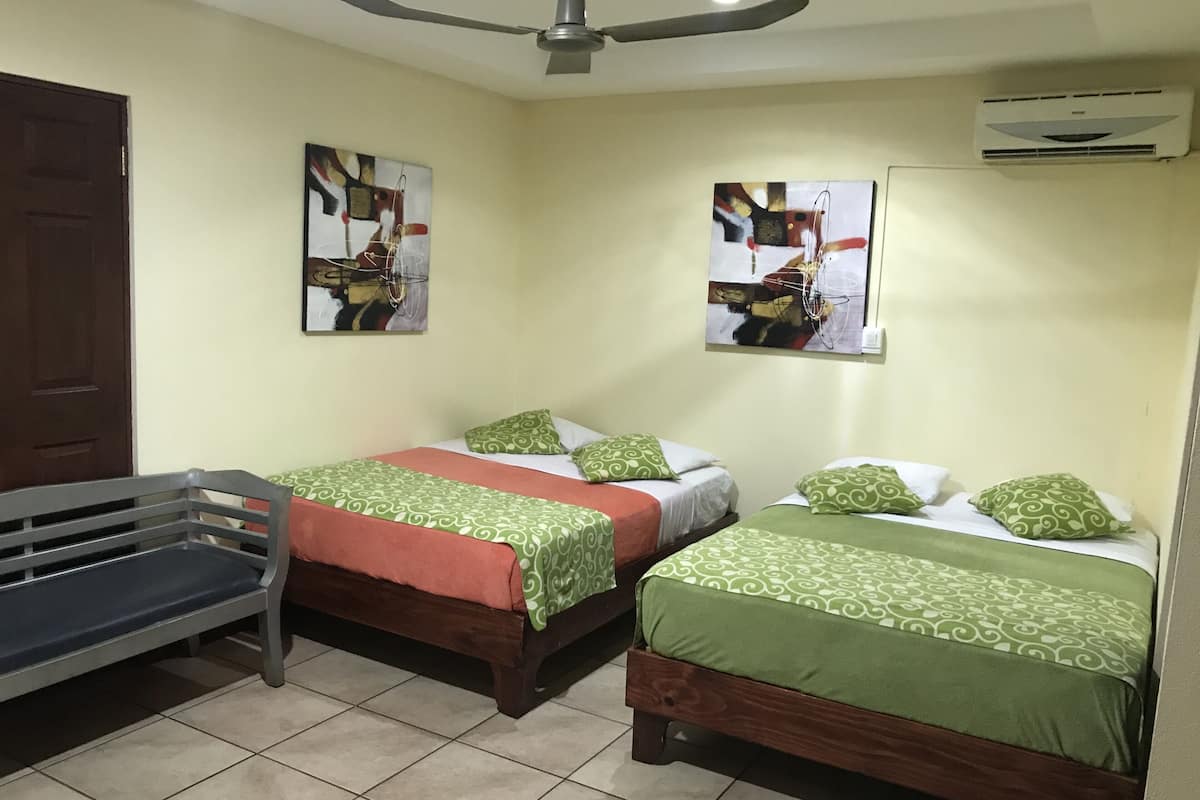 Habitación de hotel con dos camas individuales, un banco y dos cuadros abstractos en las paredes.