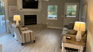 A living room with a fireplace, two armchairs, a sofa, a ceiling fan, and a TV mounted above the fireplace.