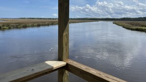 A wooden pier extending over a calm river with a clear sky and distant trees.