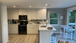 A modern kitchen with white cabinetry, a black stove, and a large window providing a view of the outdoors.