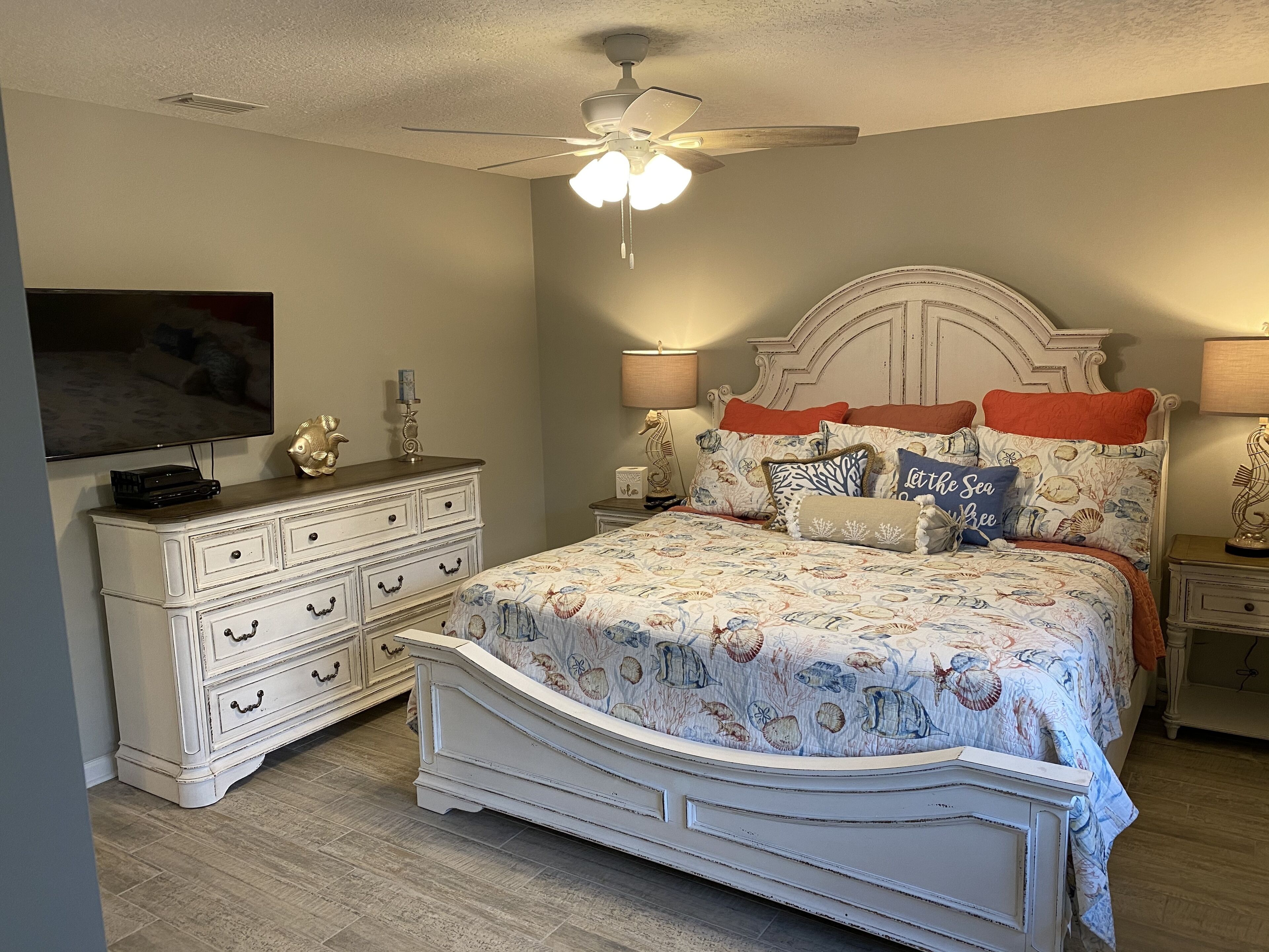 A bedroom with a bed, dresser, nightstands, and a ceiling fan.