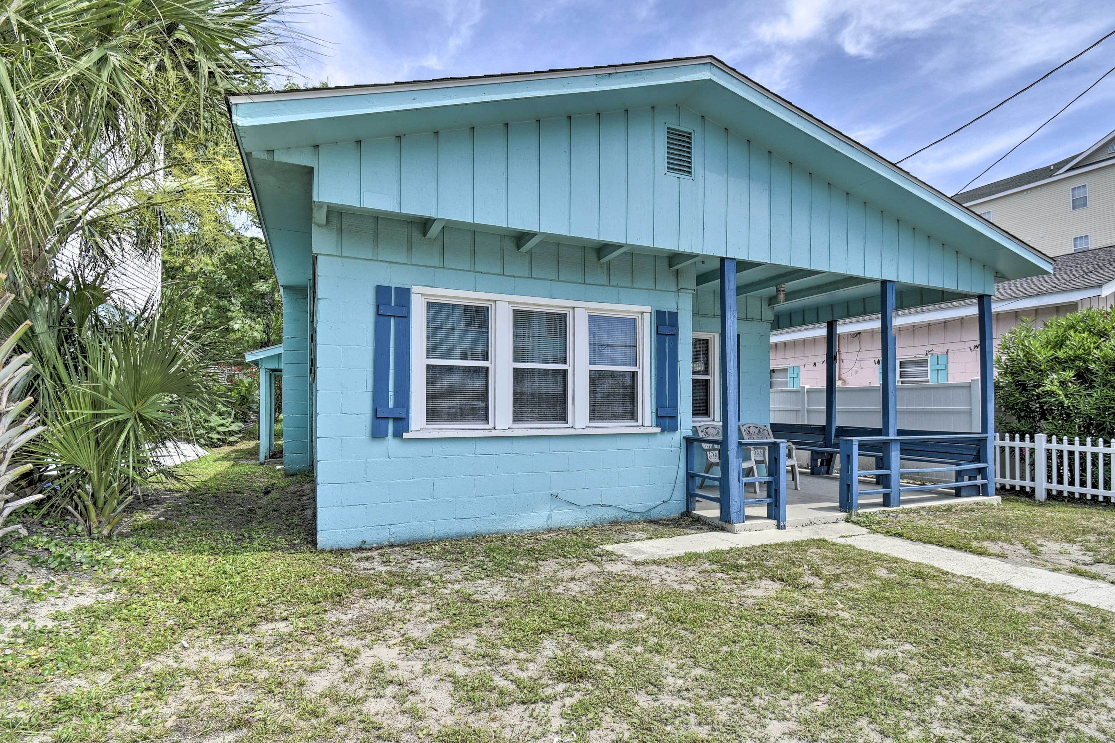 A small, single-story building with a light blue exterior and white trim. It features a covered porch with blue railings and a small set of stairs leading up to the entrance.