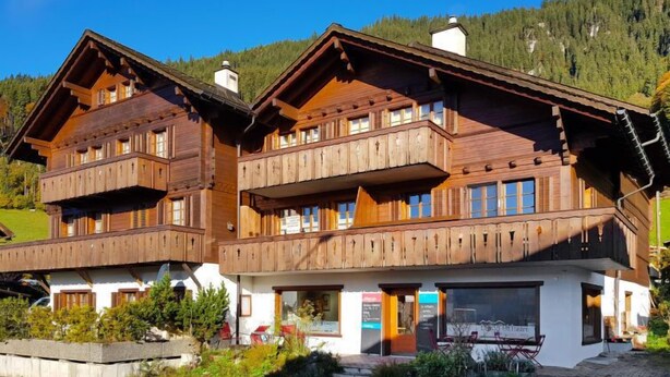 Un chalet en bois doté de balcons, un restaurant situé au rez-de-chaussée et un paysage montagneux en toile de fond.