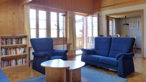 Un salon chaleureux aux murs en bois et au plafond haut, comprenant un canapé bleu, une table basse en bois et une bibliothèque remplie de livres.