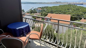 A balcony with a table and chairs, overlooking a coastal area with buildings and a ship in the distance.