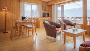 Een gezellig, houten ingerichte kamer met een eethoek, een televisie en een balkon met uitzicht op de bergen.