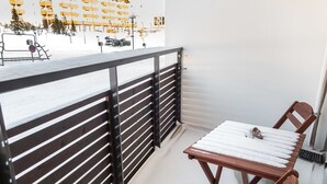 Een balkon met een houten tafel en stoelen, een metalen hekwerk en uitzicht op een gebouw met balkons.