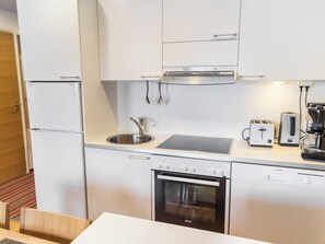 A compact kitchen with a built-in oven, a sink, a stovetop, and a coffee maker. - Nordic chalet 9209 by Interhome (Ylläsjärvi)