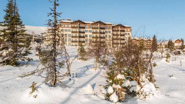 Een meerlaags hotel met balkons, omringd door met sneeuw bedekte bomen en een heldere lucht.
