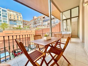A balcony with a wooden table and chairs, a view of buildings, and a car parked below. - Designer's three bedroom apartment with terrace (Barcelona)