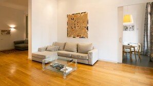 Uma sala de estar moderna com uma mesa de centro de vidro, um sofá modular bege e uma grande pintura abstrata na parede.