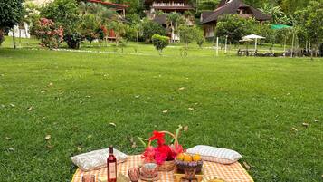 Montaje para picnic sobre un césped con manta a cuadros, cesta de picnic, botella de vino y cristalería.