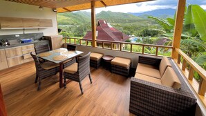 Techo de madera, una mesa de comedor con sillas, un sofá y vistas a un paisaje montañoso.
