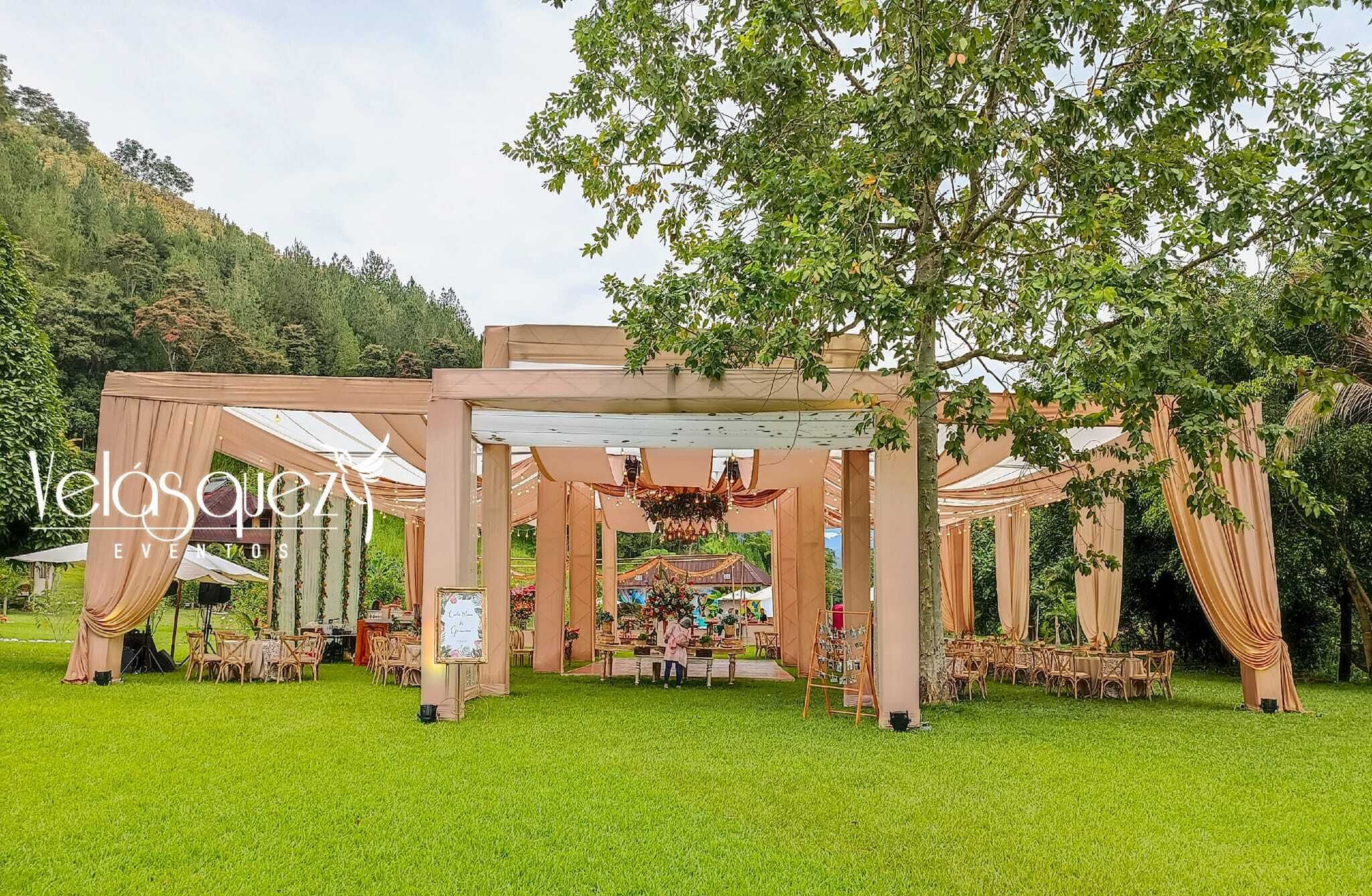 Un espacio para eventos al aire libre con zona cubierta, mesas y sillas dispuestas para una ocasión.