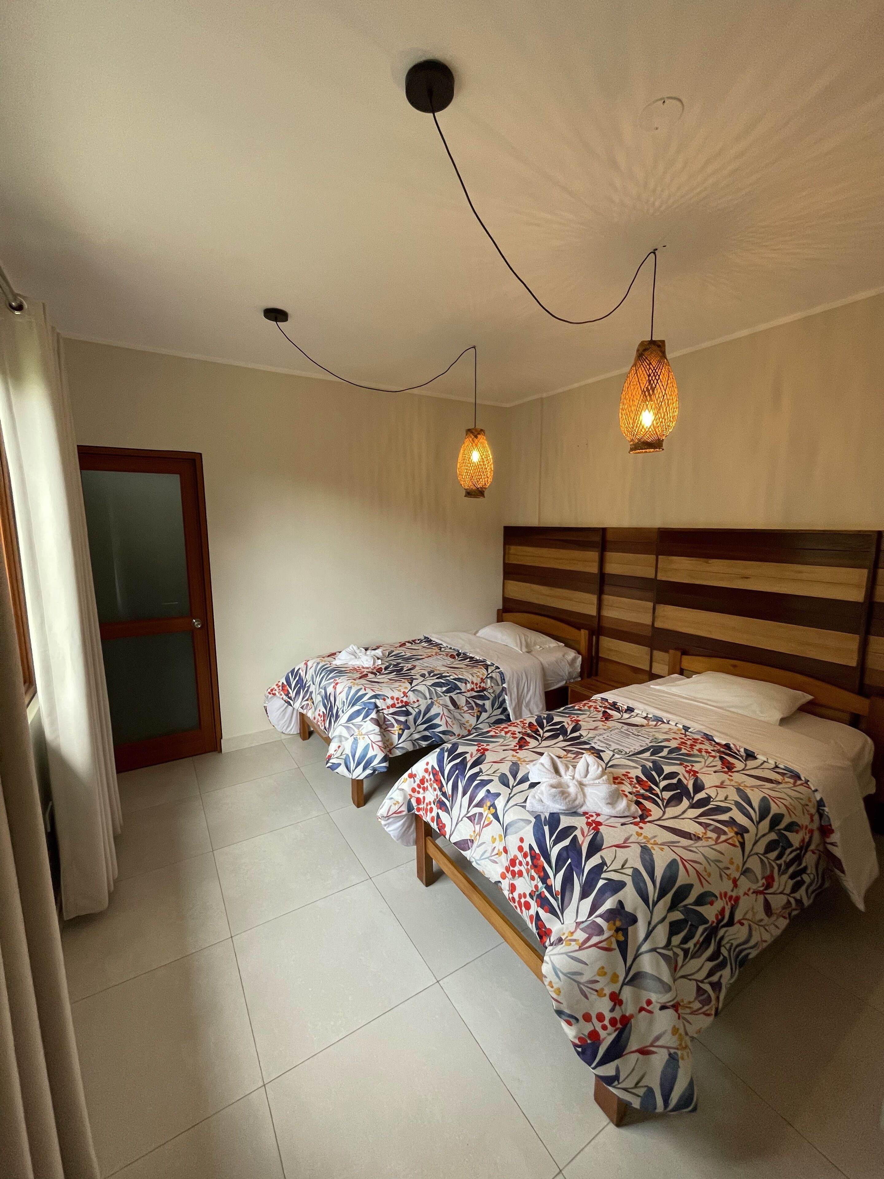 Habitación de hotel con dos camas individuales, cabecero de madera y dos lámparas colgantes.