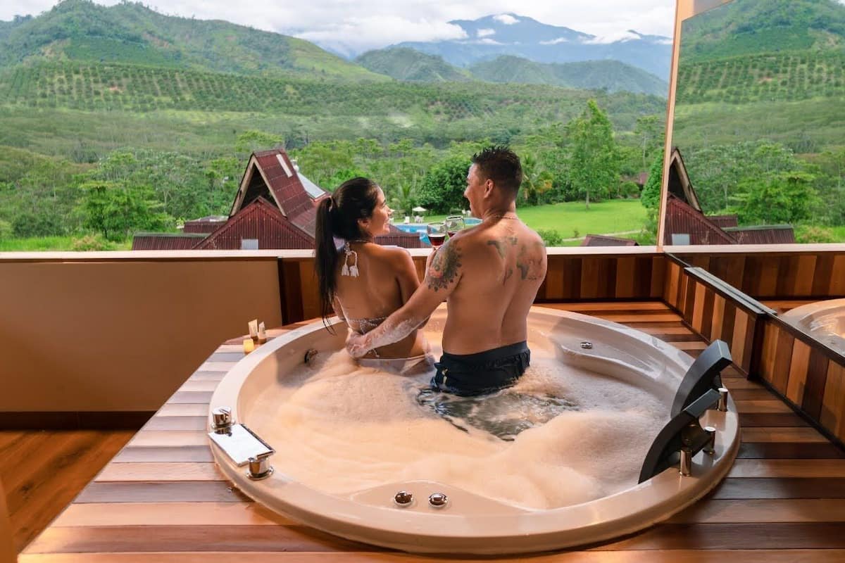 Un couple dans un bain à remous, avec une vue magnifique sur des collines verdoyantes et une terrasse en bois.