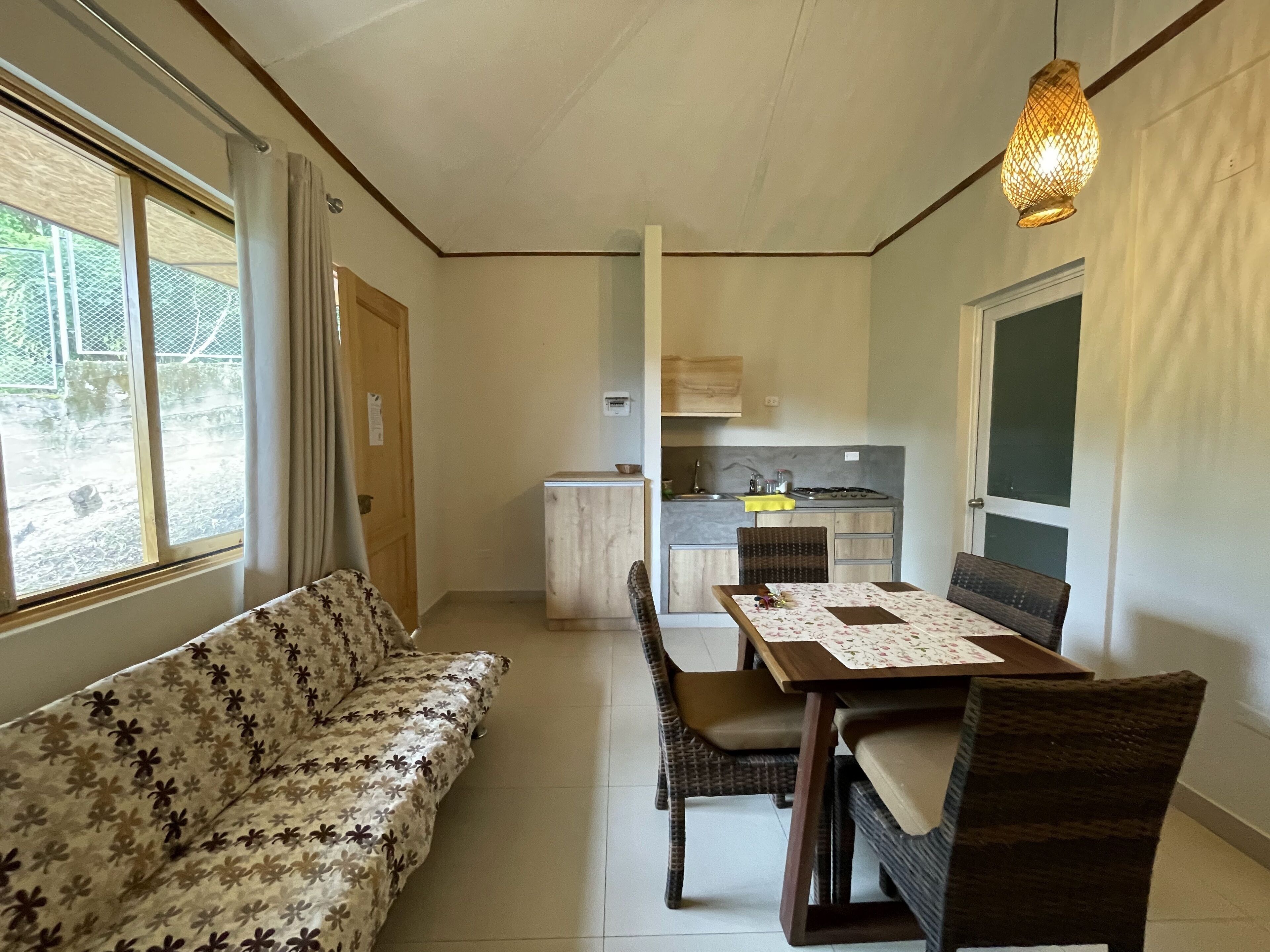 Un espace de vie compact comprenant un canapé, une table à manger, des chaises, un coin cuisine et une fenêtre avec des rideaux.