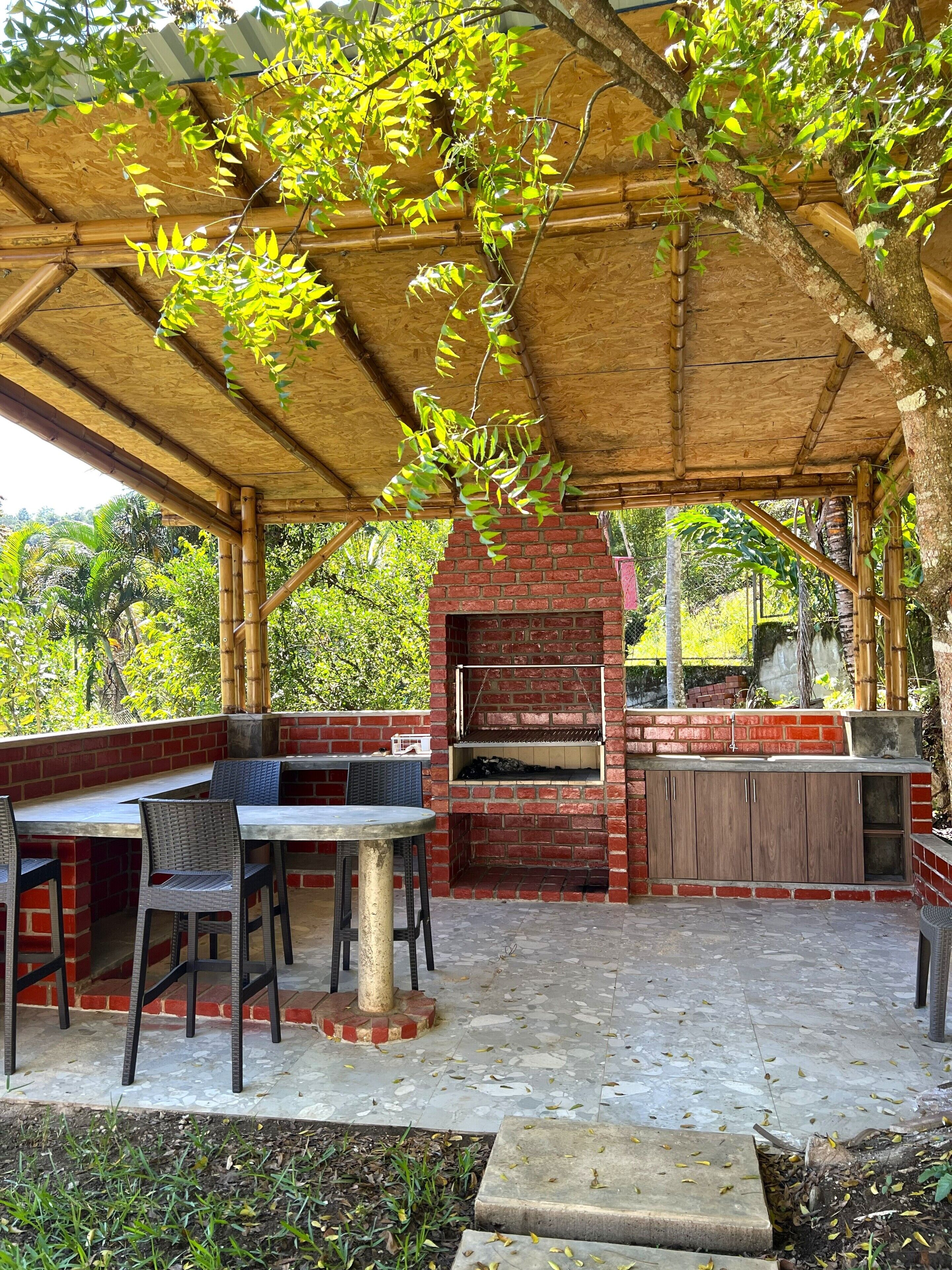 An outdoor patio with a brick barbecue, seating area, and a pergola with climbing plants.