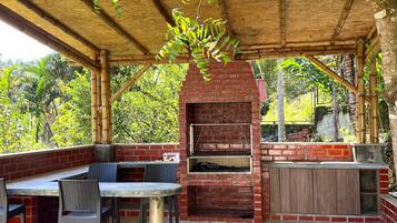 An outdoor patio with a brick barbecue, seating area, and a pergola with climbing plants.