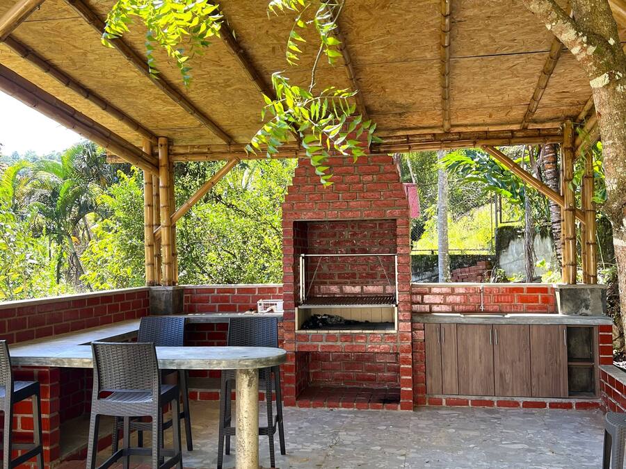 An outdoor patio with a brick barbecue, seating area, and a pergola with climbing plants.
