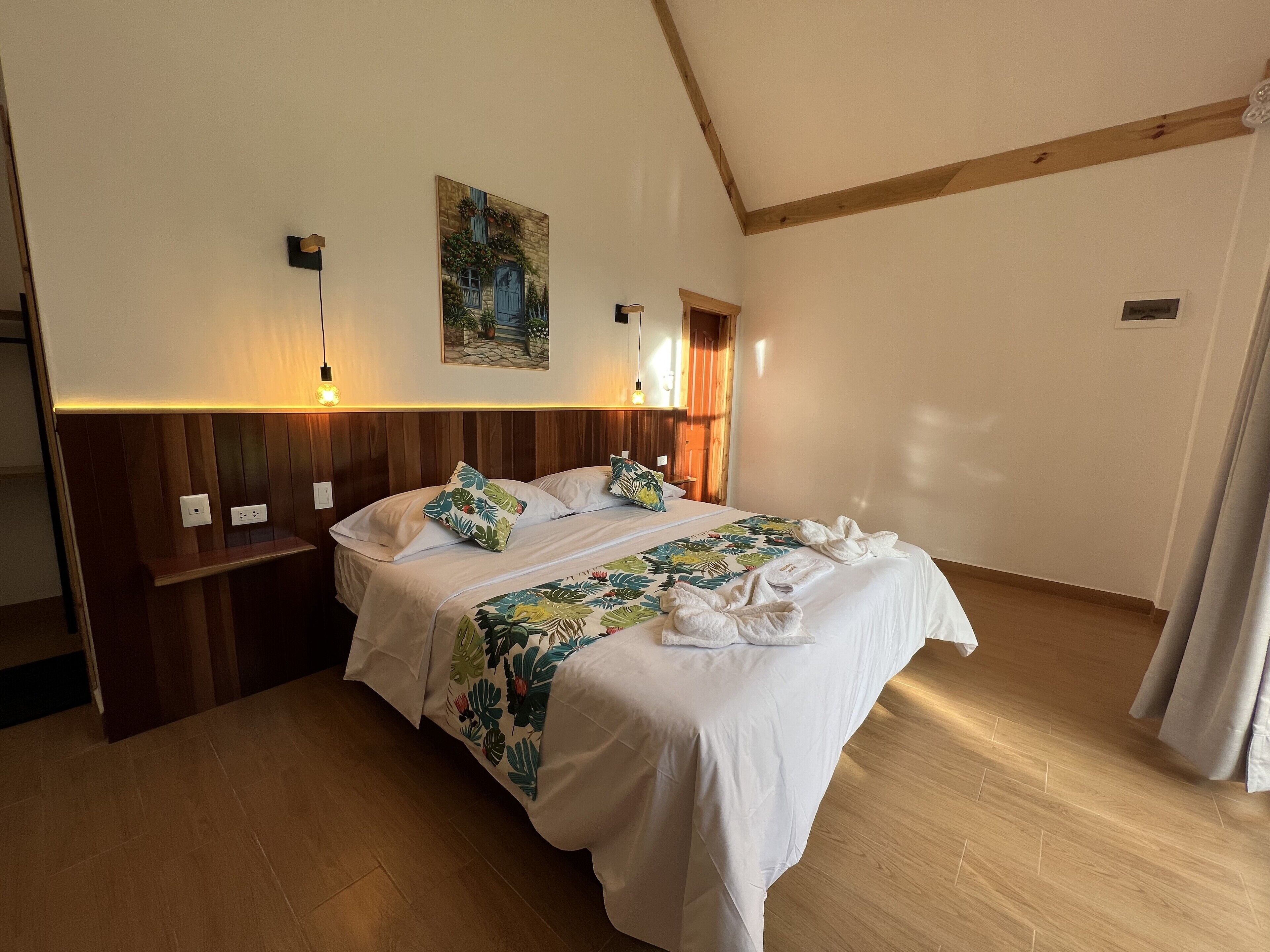 Une chambre d’hôtel avec une tête de lit en bois, un grand lit avec du linge de lit blanc, une couvre-lit à motifs floraux et deux lampes de chevet.