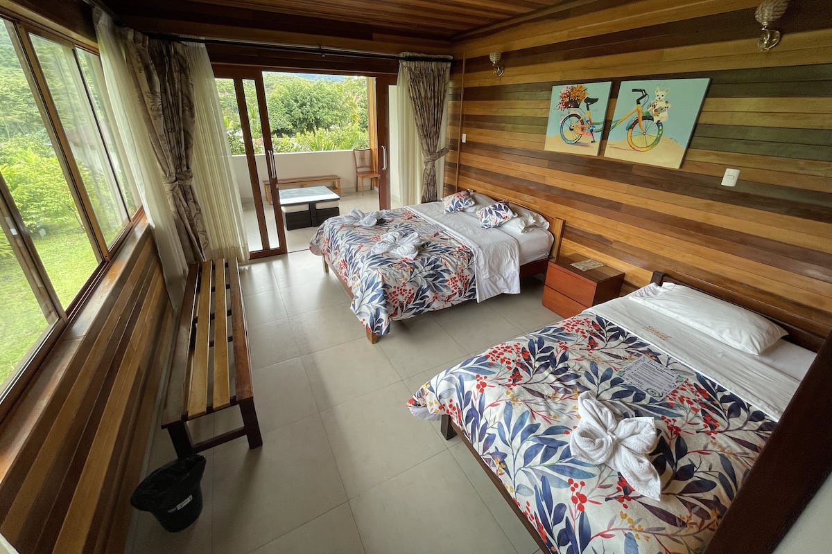 Une chambre avec deux lits, un banc et une vue sur l’extérieur.