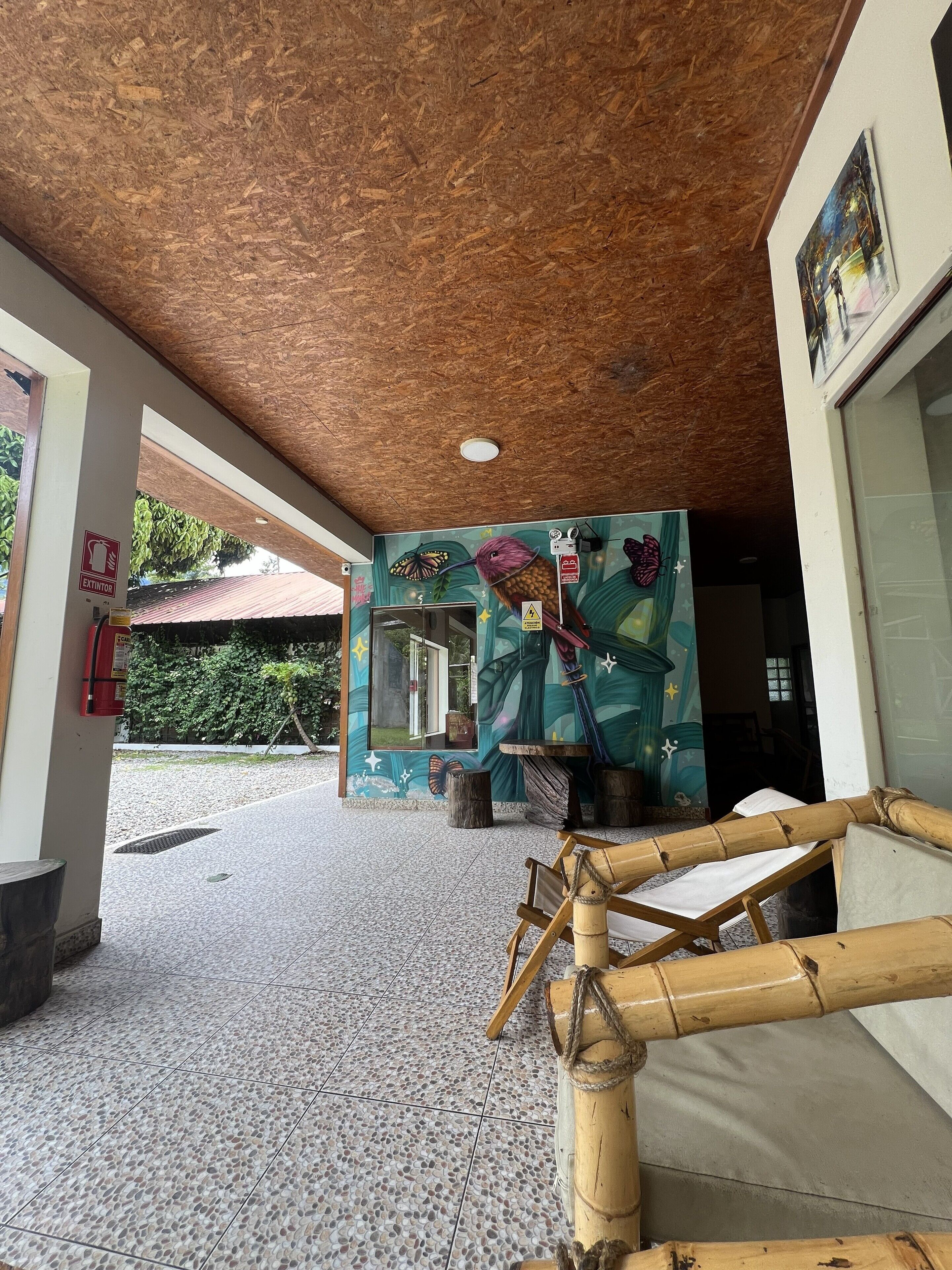 Un área de entrada techada con suelo de baldosas, techo de madera y un mural que representa un colibrí y una mariposa.
