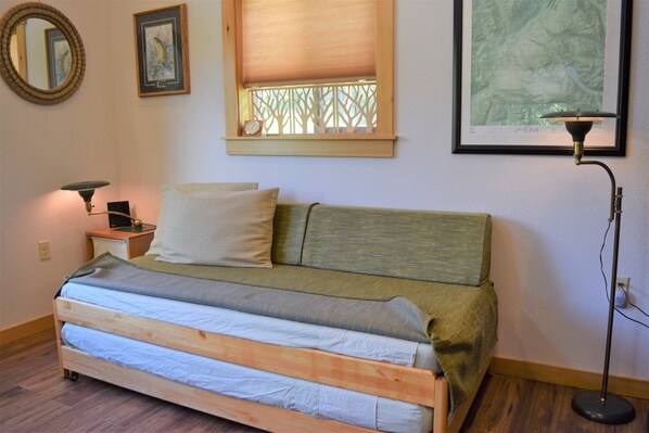A bedroom with a wooden bed, a nightstand with a lamp, a window with a wooden blind, and a framed picture on the wall. - Little Big Fish (Packwood)