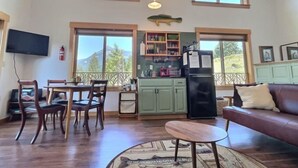 A spacious living area with a dining table, chairs, a sofa, and a kitchen area with a refrigerator and cabinets. - Little Big Fish (Packwood)