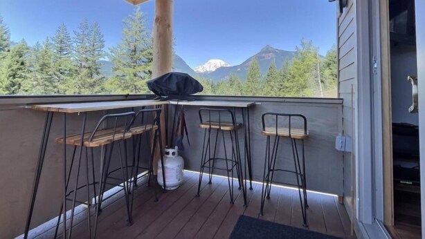 A balcony with a wooden table and two chairs, overlooking a mountainous landscape with trees. - Little Big Fish (Packwood)