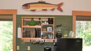 A kitchen with wooden cabinets, a black refrigerator, and a fish decoration on the wall. - Little Big Fish (Packwood)