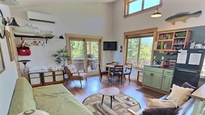 A cozy living room with a sofa, chairs, a dining table, and a kitchen area with a refrigerator and cabinets. - Little Big Fish (Packwood)