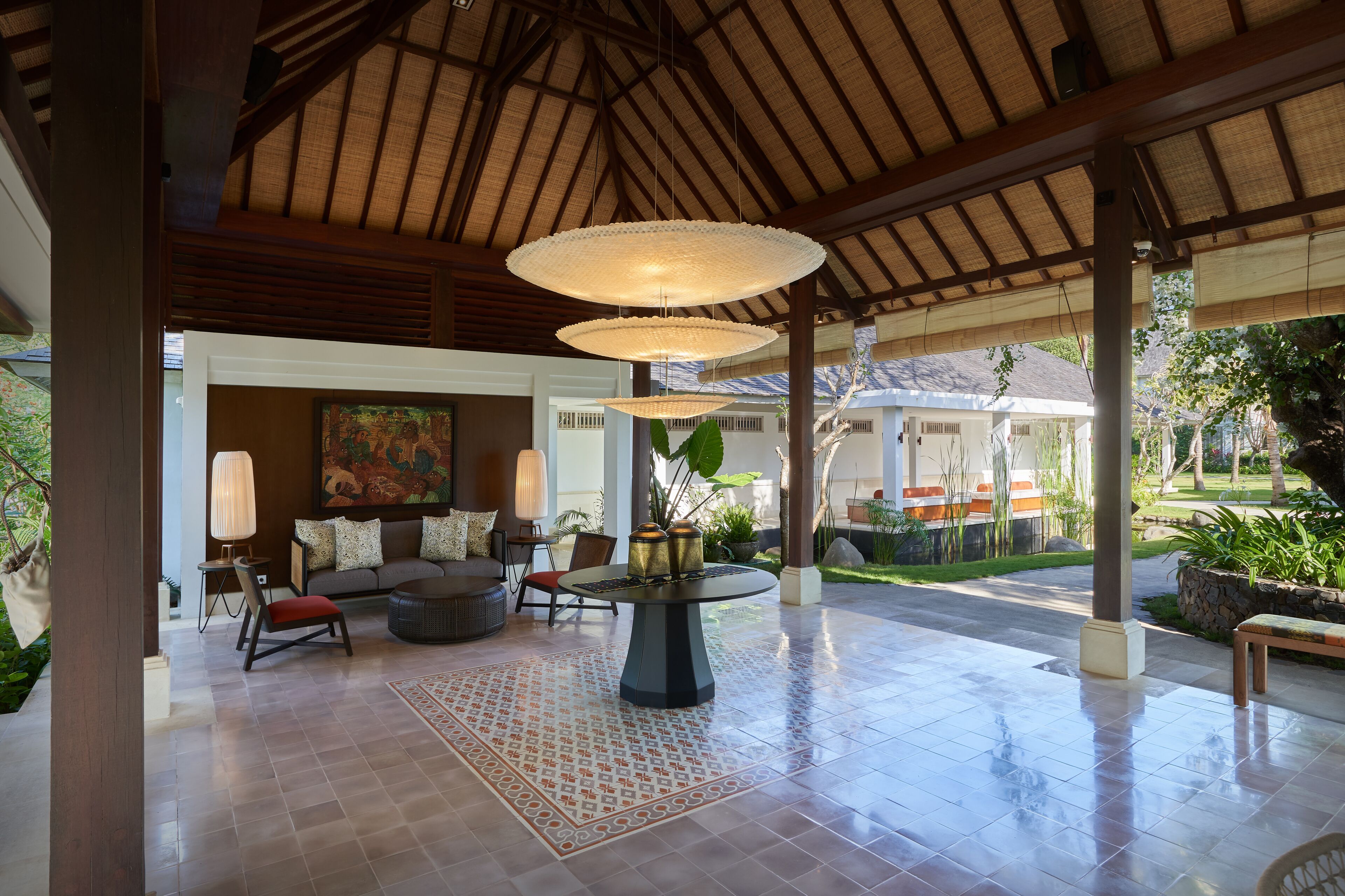 A spacious lobby with a tiled floor, a round table with decorative vases, a sofa, and a large painting.