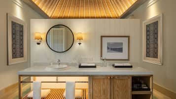 A modern bathroom with a large vanity, a wooden bench with towels, and framed artwork on the walls.