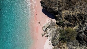 Un paysage côtier caractérisé par une plage de sable, des affleurements rocheux et une eau turquoise cristalline.