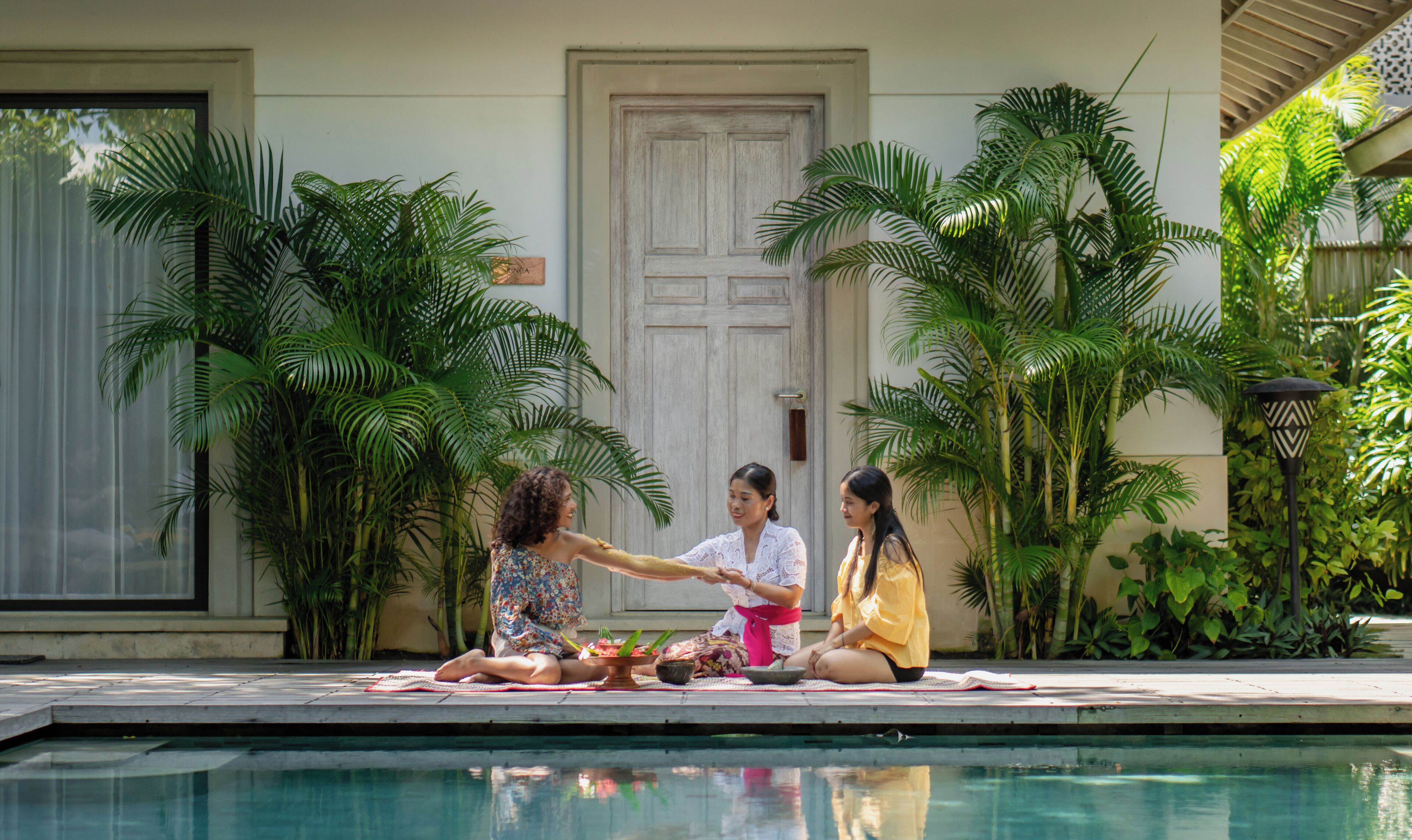 A poolside area with a tiled deck, a door, and lush greenery.