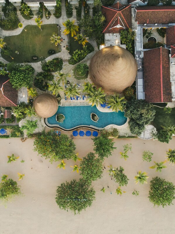 An aerial view of a resort with a large pool, palm trees, and a beach area.