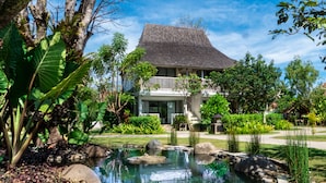 Une maison avec un grand jardin, un étang et un toit de chaume.