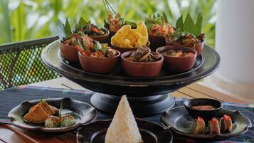 Un grand plat à étages contenant divers mets, notamment du riz, des légumes et de la viande, est posé sur une table d’où l’on peut admirer un paysage verdoyant.