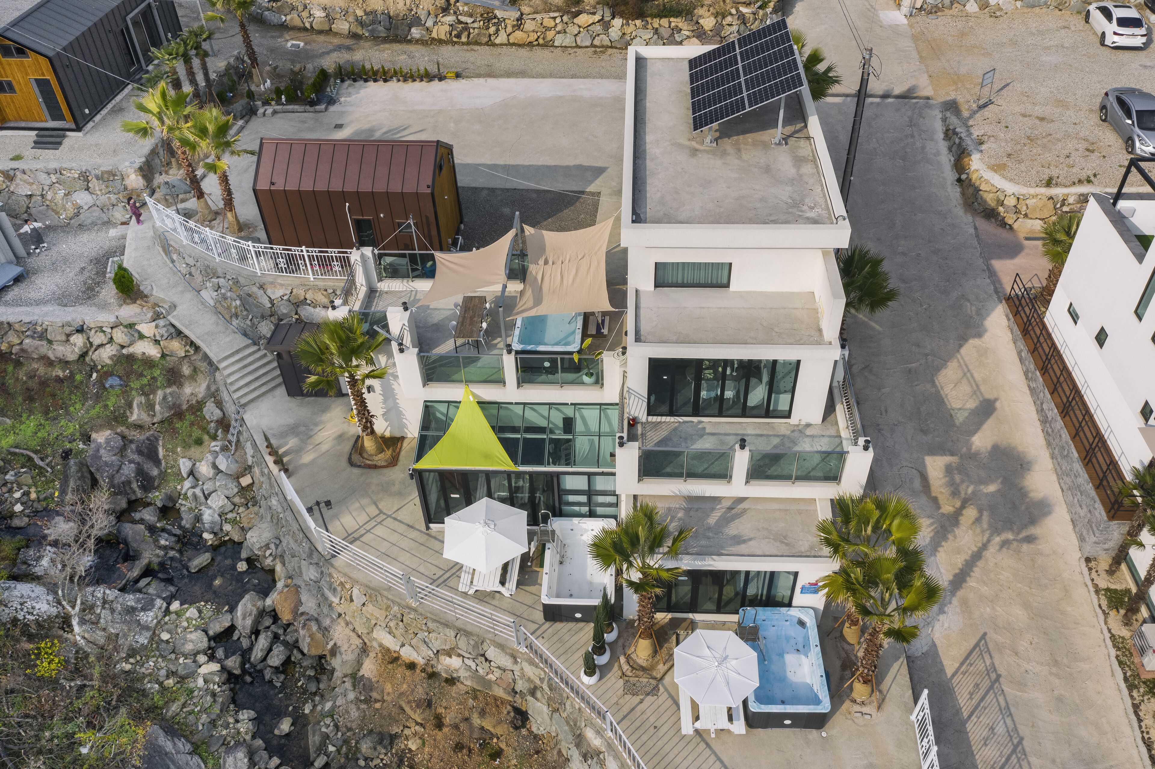 An aerial view of a modern building with a rooftop pool, a small garden area, and a stone wall.