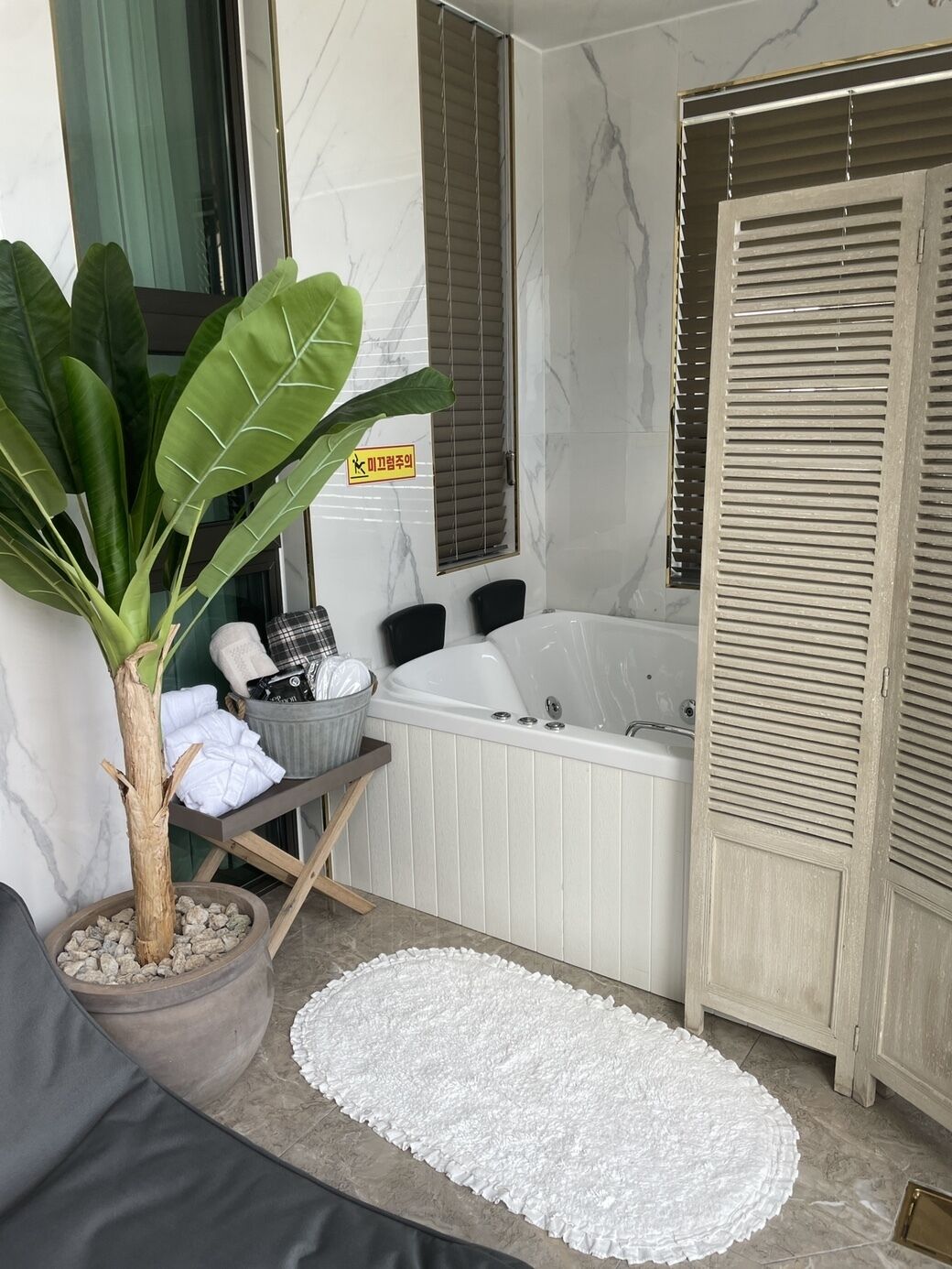 A bathroom with a bathtub, a potted plant, a towel rack, and a white rug.