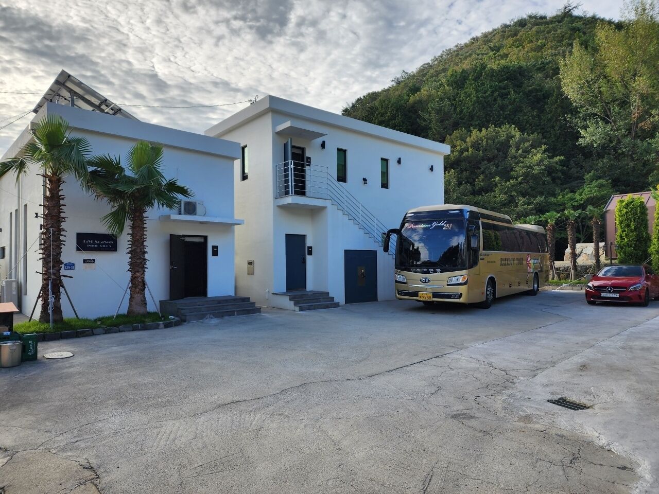 Un bâtiment moderne avec un escalier menant à un deuxième étage, un autobus garé et une voiture rouge devant.