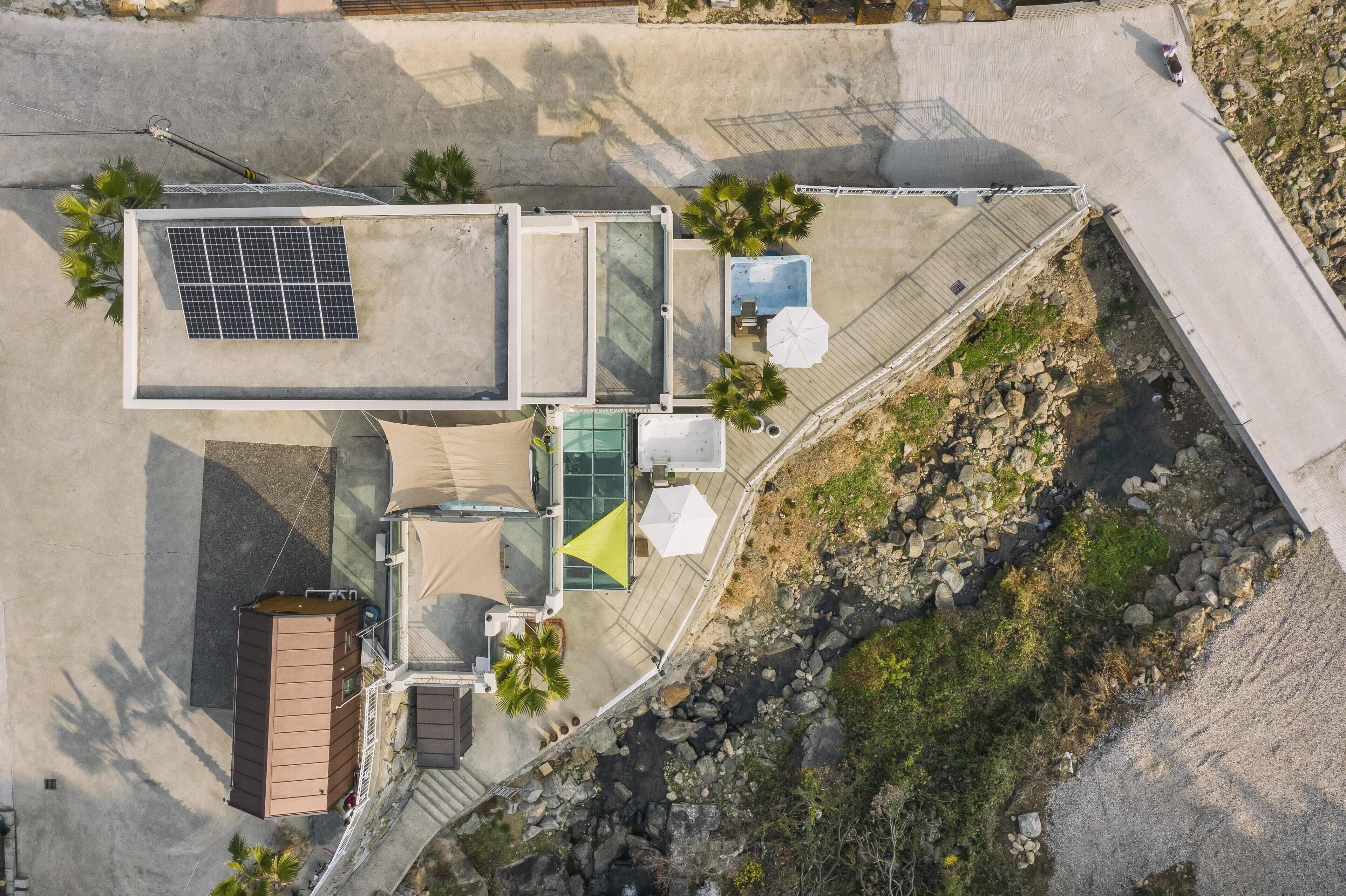 An aerial view of a rooftop terrace with a solar panel, seating areas, and a small pool.