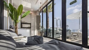 A modern living room with a large window, a sofa, a potted plant, and a view of the outside. - Lim Sea Side Poolvilla Pension (Namhae)